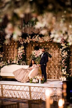 a man and woman standing next to each other in front of a bed with flowers on it