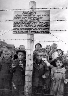 an old black and white photo of children behind a barbed wire fence with a sign on it