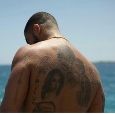 a man with tattoos on his back standing in front of the ocean