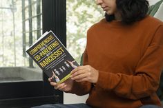 a woman sitting on a couch holding a book in her hands and looking at it