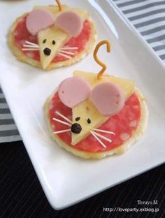 two small pizzas with cheese and ham in the shape of mice on white plates