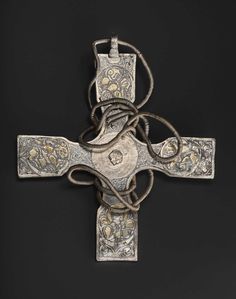 an old silver cross with intricate designs on it's sides and two cords hanging off the side