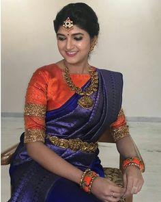 a woman sitting in a chair wearing an orange and blue sari with gold jewelry