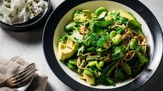 a bowl filled with broccoli and noodles next to a plate of mashed potatoes