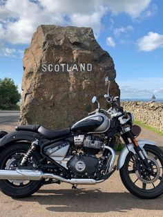 a motorcycle parked next to a large rock on the side of a road with scotland written on it