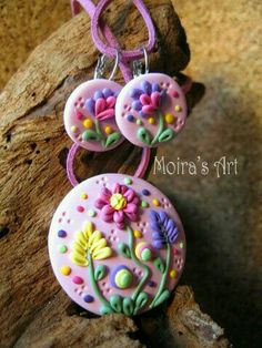 two pink buttons with flowers on them hanging from a purple cord and attached to a rock