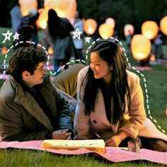 a man and woman sitting on the grass with paper lanterns in the background