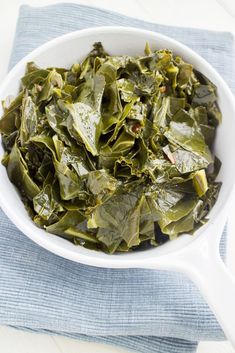 a white bowl filled with collard greens on top of a blue napkin