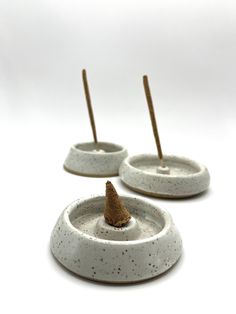 three small white bowls with wooden sticks sticking out of the top one is filled with sand