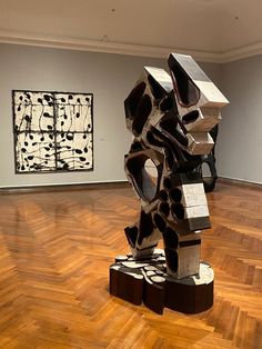 an abstract sculpture is in the middle of a room with wood floors and paintings on the walls