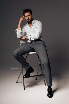 a man sitting on top of a chair wearing a white shirt and gray pants with his hands in his pockets