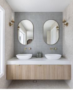 two round mirrors are above the sinks in this modern bathroom with wood cabinets and white countertops