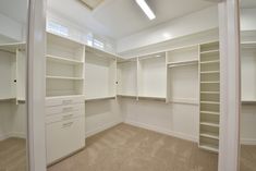 an empty white closet with shelves and drawers on the wall next to carpeted floor