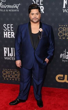 a man in a blue suit and black shirt on the red carpet at an awards event