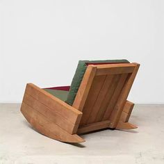 a wooden chair sitting on top of a cement floor next to a white wall with a green cushion