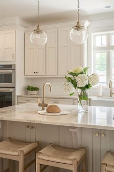 a kitchen with white cabinets and marble counter tops, two pendant lights over the island