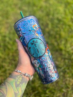 a person's hand holding a starbucks cup in the grass with tattoos on it