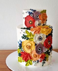 a multi - tiered cake decorated with colorful flowers on a white plate and wooden table