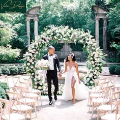 a bride and groom holding hands in front of an arch with flowers on it at their wedding