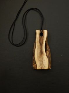 a wooden pendant with a black cord on a table next to a piece of wood