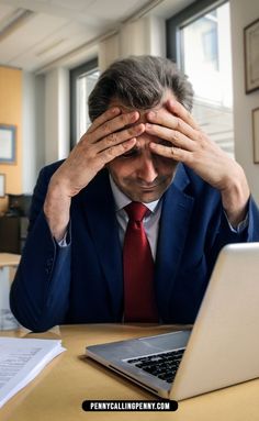 a man in a suit and tie sitting at a desk with his hands on his head