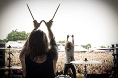 two people on stage with their hands in the air and one person holding drums behind them