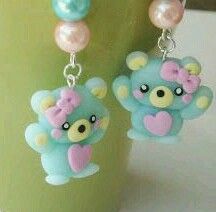 two blue teddy bears with pink bows and pearls on their earring hooks are sitting next to each other