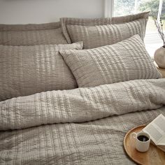 a coffee cup on a tray next to a bed with beige quilts and pillows