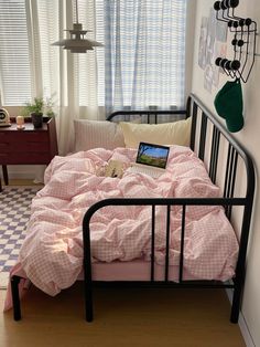 a bed with pink sheets and pillows in a small room next to a checkered floor