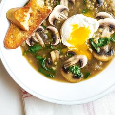 a bowl of soup with mushrooms, spinach and an egg in it on a white plate