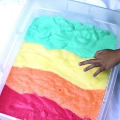 someone is holding their hand over a rainbow cake