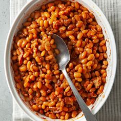 a white bowl filled with baked beans on top of a table next to a spoon