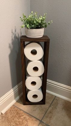 three rolls of toilet paper are stacked up on a stand next to a potted plant