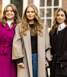 three women standing next to each other in front of a building wearing coats and jeans