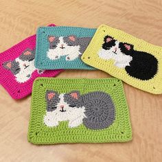 four crocheted coasters with cats on them sitting on a wooden table top