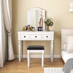 a white dressing table with a mirror, stool and flowers on it in a bedroom