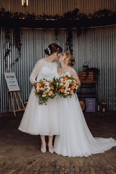 two women in white dresses standing next to each other and one is kissing the other