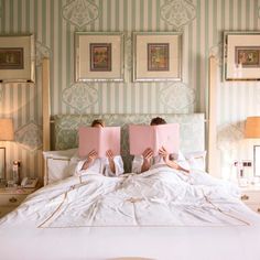 two people laying in bed with pink books on their backs, one reading a book