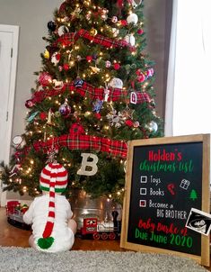 a christmas tree is decorated with plaid stockings and other holiday decorations in front of a chalkboard sign