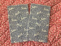 two blue and white napkins sitting on top of a red bedspread covered in flowers