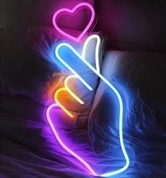 a neon sign that looks like a hand holding a heart on top of a pillow