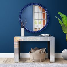 a blue wall with a mirror and basket on the floor next to it, in front of a plant