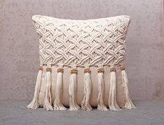 a white pillow with tassels on the front and back of it, sitting against a wall