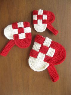 three crocheted red and white mitts sitting on top of a wooden table