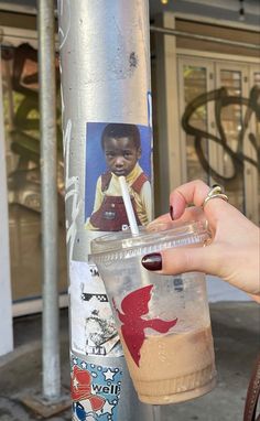 a person holding a drink in front of a pole