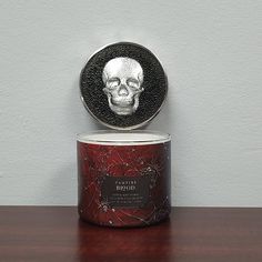 a tin with a skull on it sitting on top of a wooden table next to a white wall