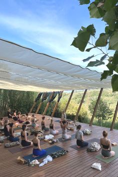 a group of people sitting on top of a wooden floor in yoga mats under a tent