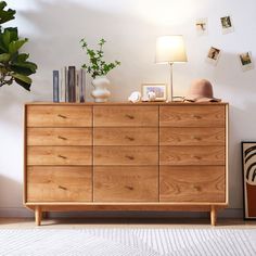 a wooden dresser sitting in a room next to a lamp and pictures on the wall