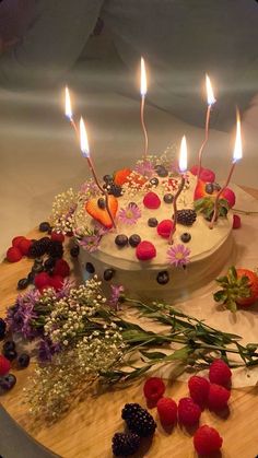 a birthday cake with lit candles surrounded by flowers and berries