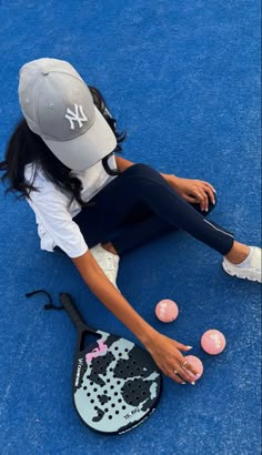 a young woman sitting on the ground with her tennis racket and balls in front of her